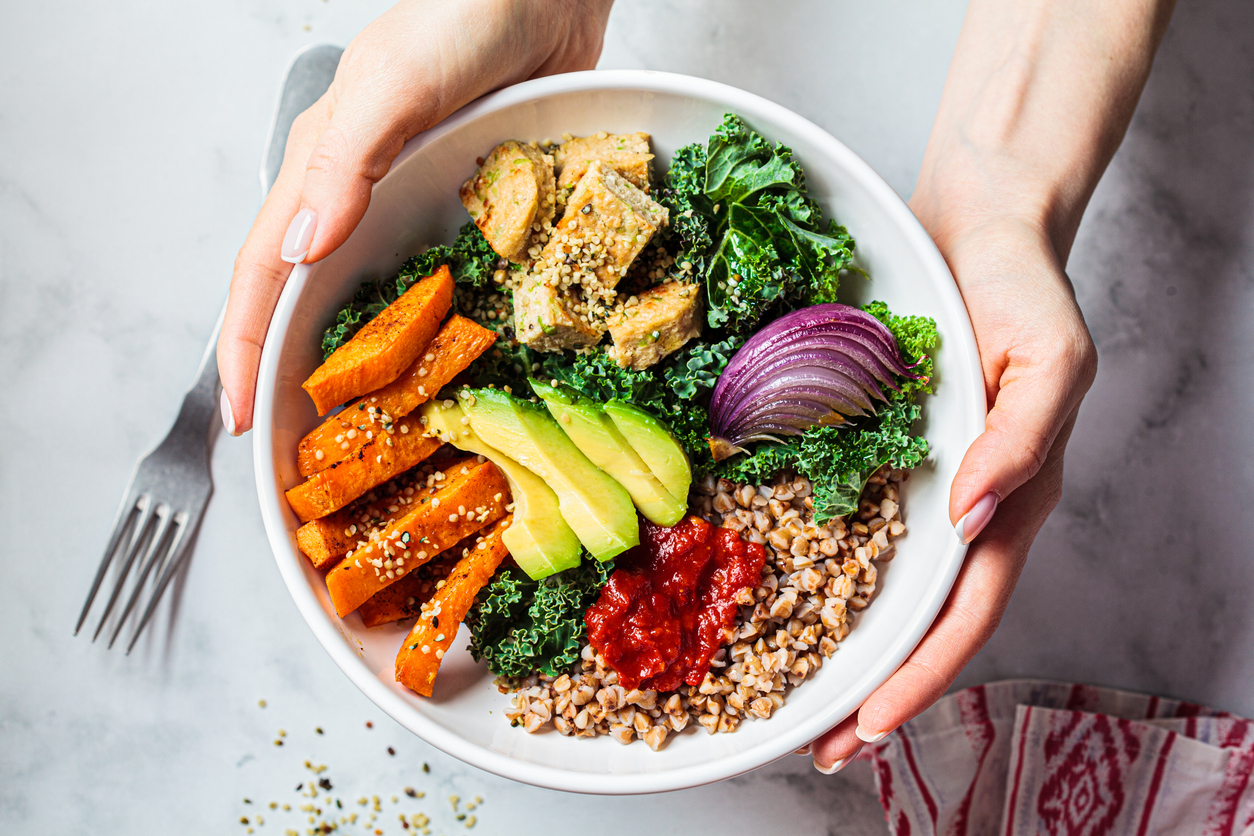 Vegan lunch salad with kale, baked sweet potato, tofu, buckwheat and avocado in a white bowl