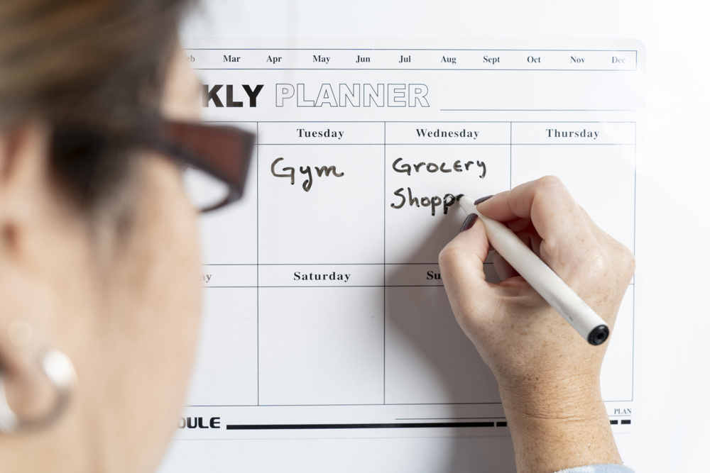 Woman writing daily tasks on a magnetic weekly planner stuck to the refrigerator