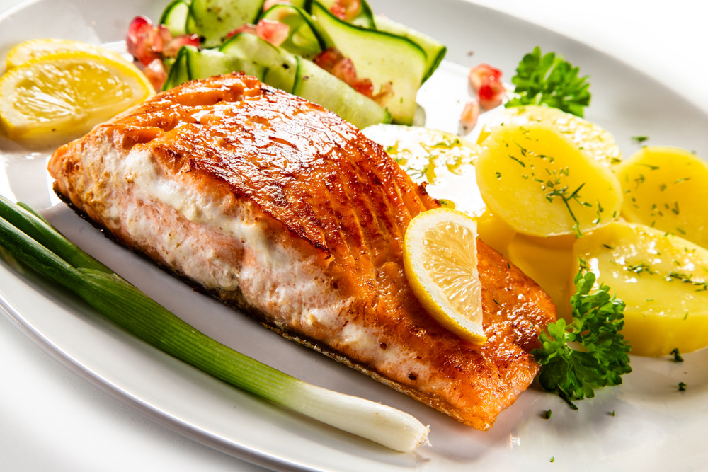 Fried salmon steak with boiled potatoes and lemon served on white plate on white background